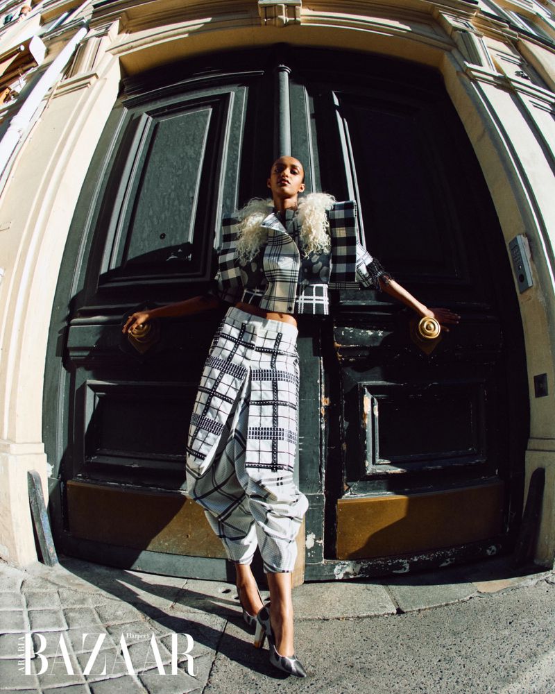 Model Muna Mahamed in a black and white plaid suit posing against large dark doors for Harper's Bazaar Arabia.