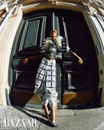 Model Muna Mahamed in a black and white plaid suit posing against large dark doors for Harper's Bazaar Arabia.