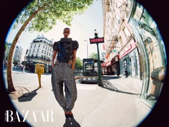 Muna Mahamed posing on a Parisian street in a black structured puff-sleeve top and patterned trousers next to a Metro sign.