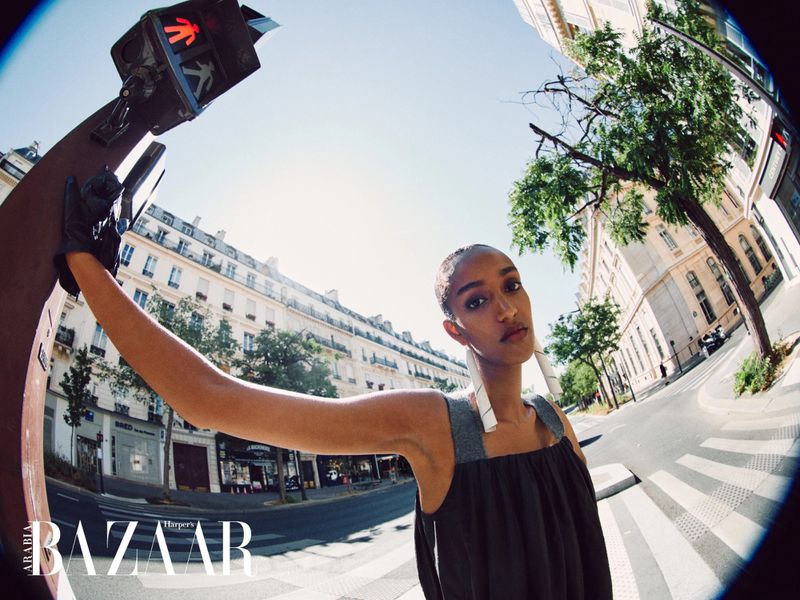 Model Muna Mahamed leaning against a pedestrian traffic signal on a city street through a fisheye lens.