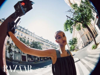 Model Muna Mahamed leaning against a pedestrian traffic signal on a city street through a fisheye lens.