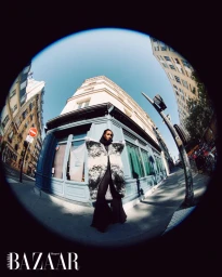 Model Muna Mahamed in an oversized black and white coat posing on an urban street corner, captured in a circular fisheye lens.