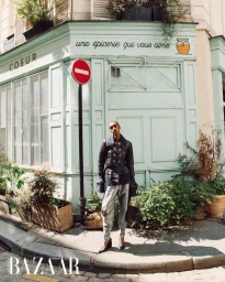 Model Muna Mahamed in a black quilted jacket and silver trousers standing outside a mint green Parisian storefront.