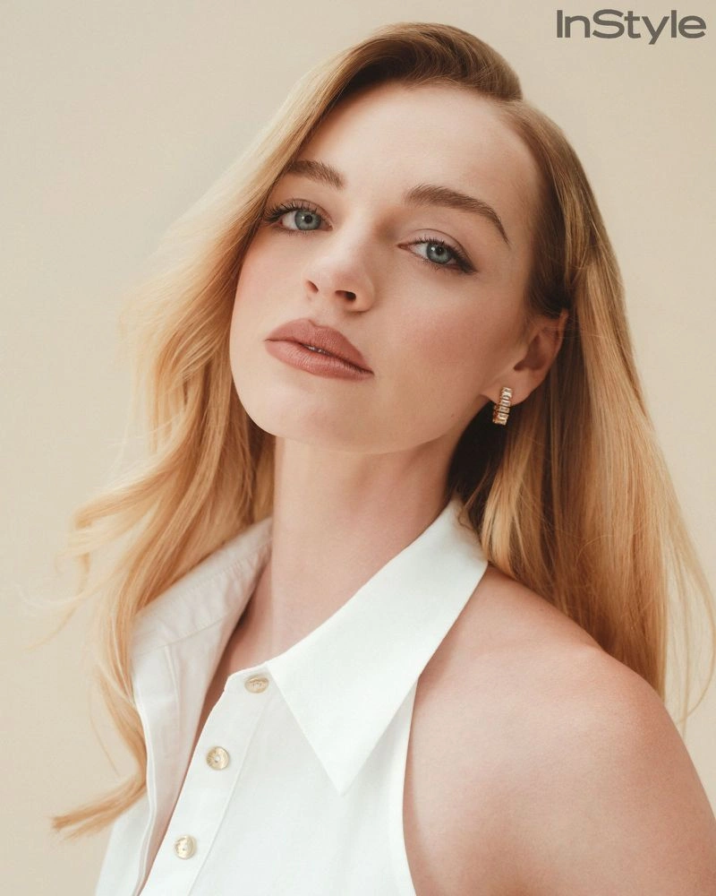 Iris Apatow posing in a white sleeveless button-up collared top against a warm neutral studio backdrop.