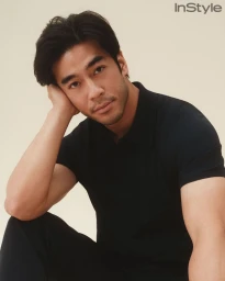 Man in a black polo shirt resting his head against his hand against a neutral studio backdrop for InStyle.