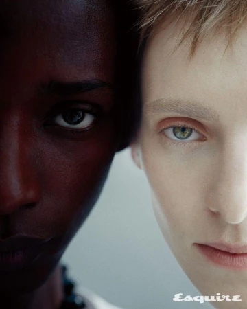 Extreme close-up split portrait of two models, one Black and one fair-skinned with light eyes, gazing forward.