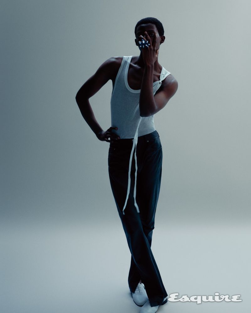 Model Gideon Adeniyi posing in a white tank top and black trousers against a pale studio backdrop for Esquire Korea.