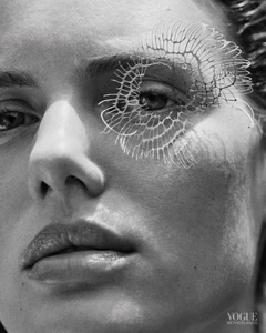 Black and white close-up portrait of a woman's face featuring an intricate organic lattice structure placed over her eye.