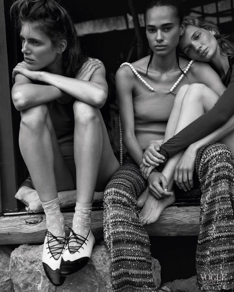 Three female models seated together in textured knitwear and pearl-embellished fashion in a black-and-white editorial portrait.