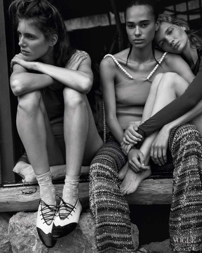 Three female models seated together in textured knitwear and pearl-embellished fashion in a black-and-white editorial portrait.