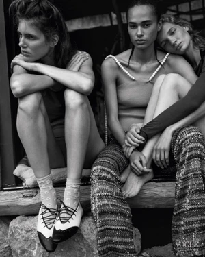 Three female models seated together in textured knitwear and pearl-embellished fashion in a black-and-white editorial portrait.
