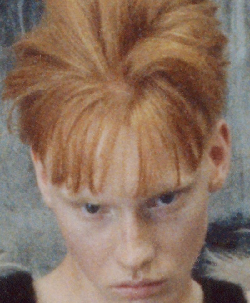 Close-up portrait of a fair-skinned model with styled spiky red hair and front bangs looking directly forward.