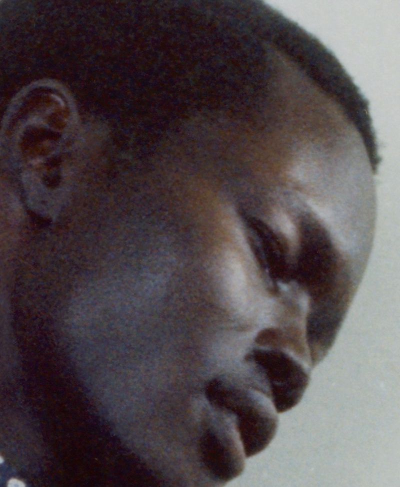 Close-up profile portrait of a Black man looking downward against a neutral grey background.