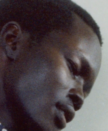 Close-up profile portrait of a Black man looking downward against a neutral grey background.