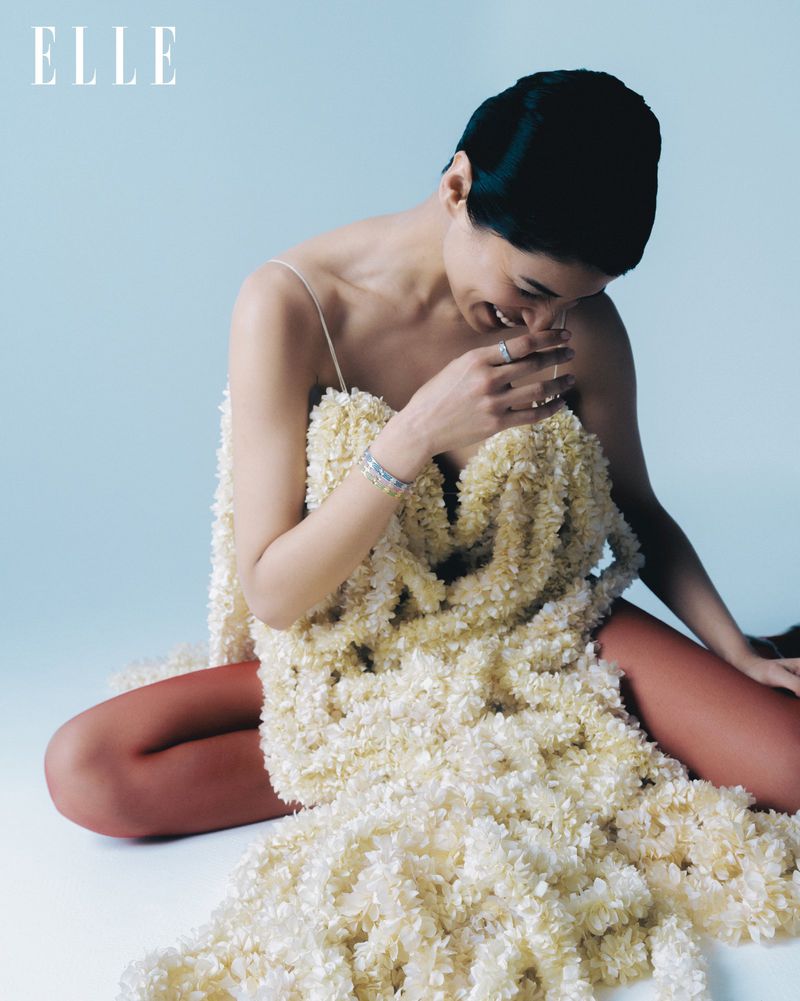 Kirandeep Chahal sitting in a textured cream ruffled dress for Elle India against a pale blue studio background.