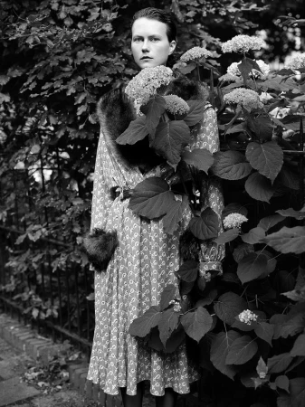 Model Julie Hoomans in a patterned long dress with fur accents standing amid hydrangea bushes in a black and white fashion portrait.