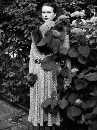 Model Julie Hoomans in a patterned long dress with fur accents standing amid hydrangea bushes in a black and white fashion portrait.