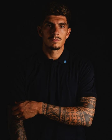 Footballer Giovanni Di Lorenzo wearing a navy Emporio Armani polo shirt with sleeve tattoos against a black studio backdrop.