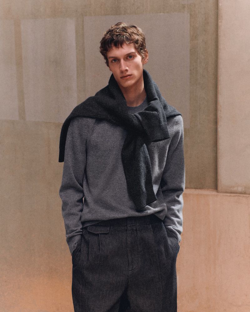 Model Leonard Kipker wearing a grey crewneck sweater with a dark jumper tied around his neck in the COS F/W 26 campaign.