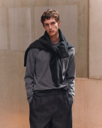 Model Leonard Kipker wearing a grey crewneck sweater with a dark jumper tied around his neck in the COS F/W 26 campaign.