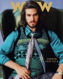 Actor Andrew Garfield sitting in a green leather wingback armchair wearing a teal satin shirt and patterned knit vest.