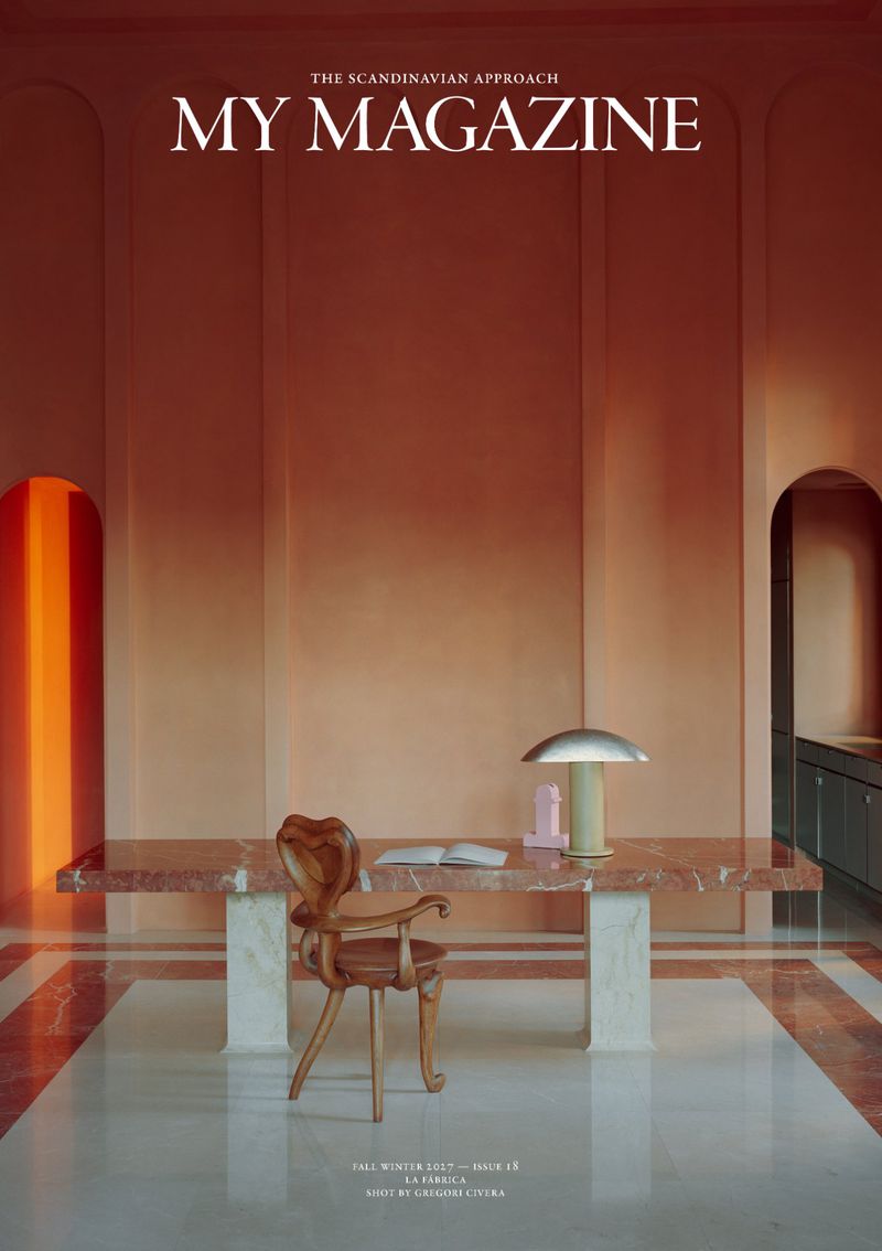 Architectural interior magazine cover featuring a marble desk, carved wooden chair, and dome table lamp against terracotta walls.
