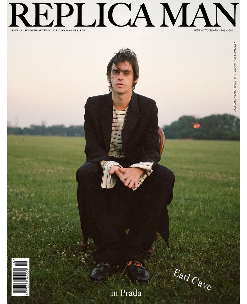 Actor Earl Cave seated on a chair in an open grassy field wearing a black suit for the cover of Replica Man Magazine.