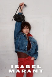 Model Mathilda Gvarliani holding a black handbag overhead wearing a denim jacket and red pants against a white wall.