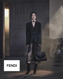 Tang Yan poses in a black blazer and lace skirt holding a black Fendi Peekaboo handbag on a dimly lit set with atmospheric haze.