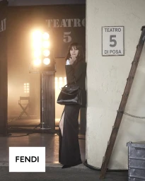 Monica Bellucci in a black blazer and slit skirt holding a black Fendi Peekaboo bag on a soundstage set.