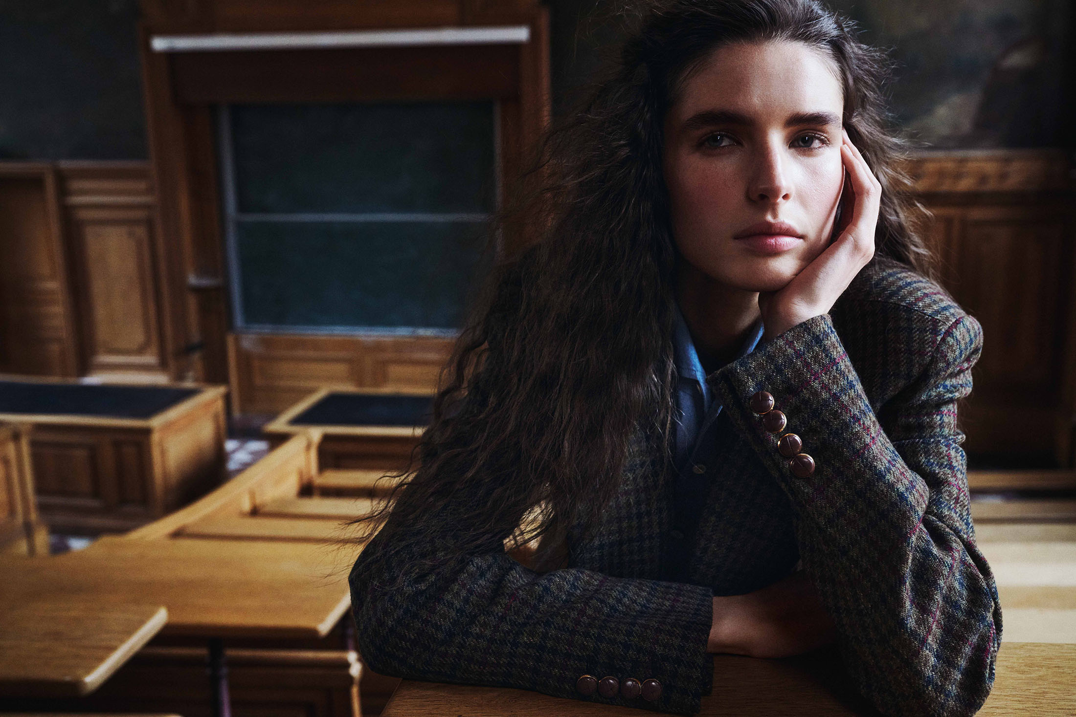 Model Libby Taverner resting her chin on her hand wearing a tweed blazer in a wooden lecture hall for Loro Piana.