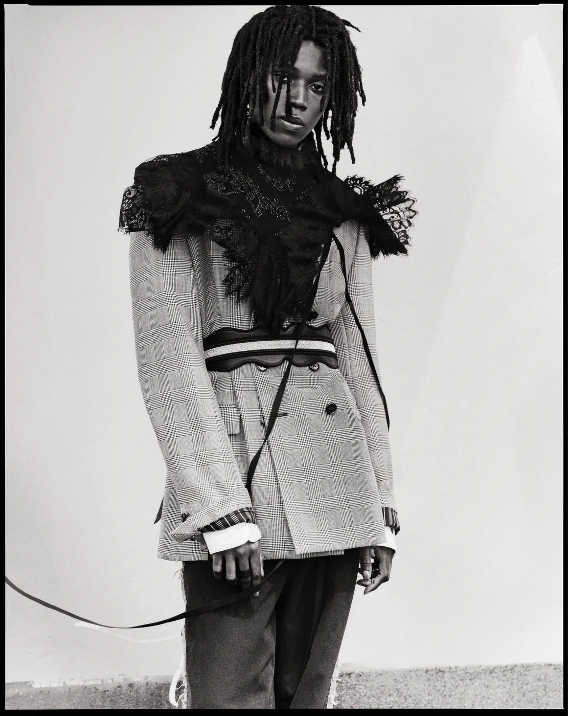Model Ezekiel Conteh wearing a light tailored blazer with a black lace shoulder overlay and belt for Ann Demeulemeester.