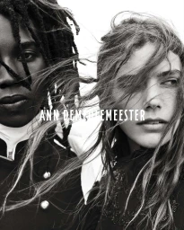 Monochrome close-up of two models with windswept hair wearing high-collared dark coats for Ann Demeulemeester.