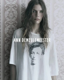 Model wearing an oversized white graphic t-shirt against patterned damask wallpaper in an Ann Demeulemeester campaign.