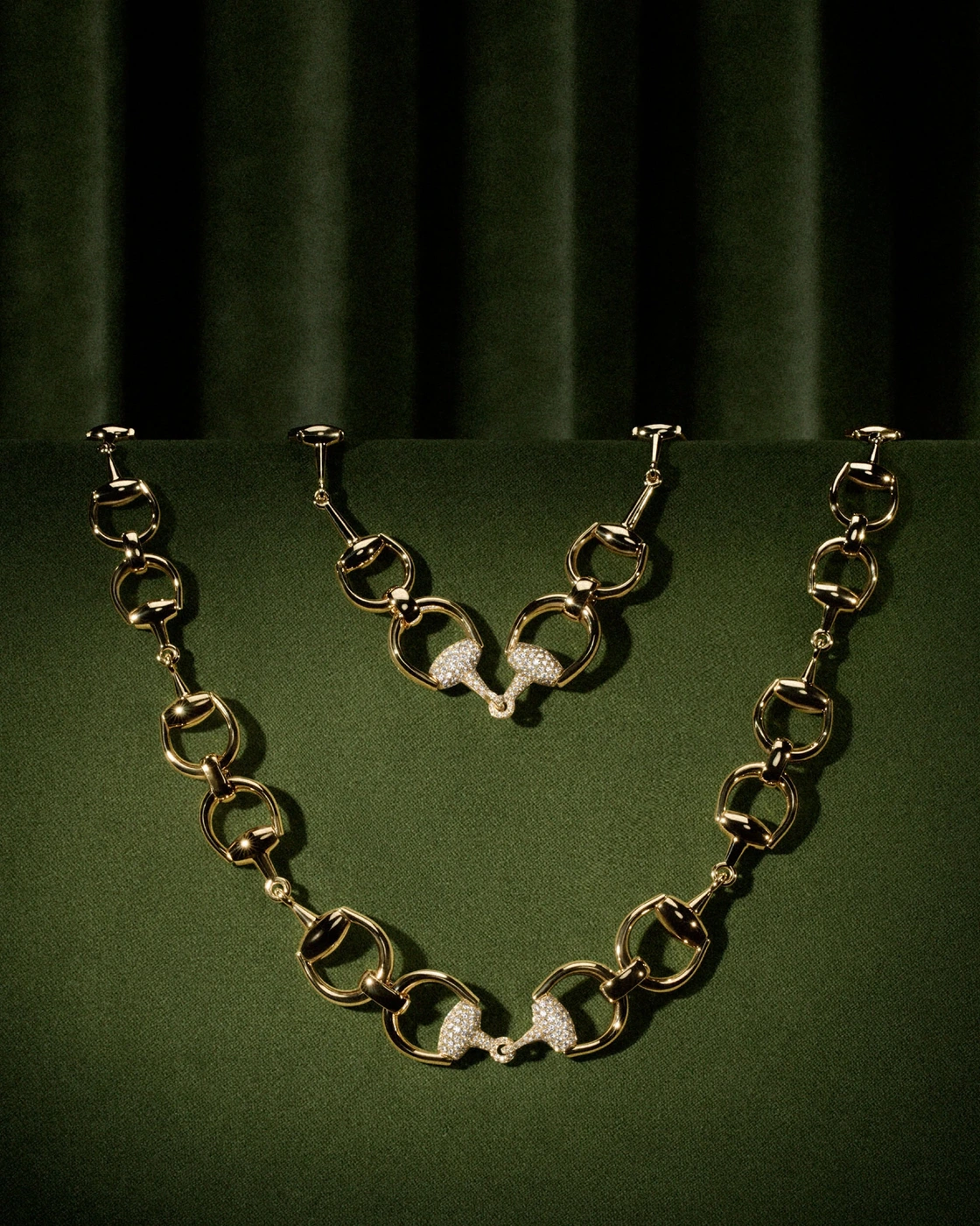 Gold horsebit chain necklace with pavé diamond accents draped over olive green velvet.