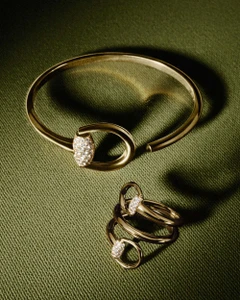 Gucci gold Horsebit cuff bracelet and matching spiral diamond ring displayed on olive green textured fabric.