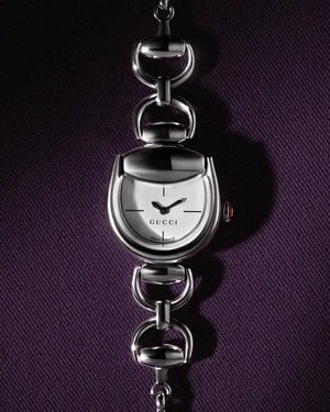 Close-up of a silver Gucci Horsebit watch on a textured dark purple fabric backdrop.