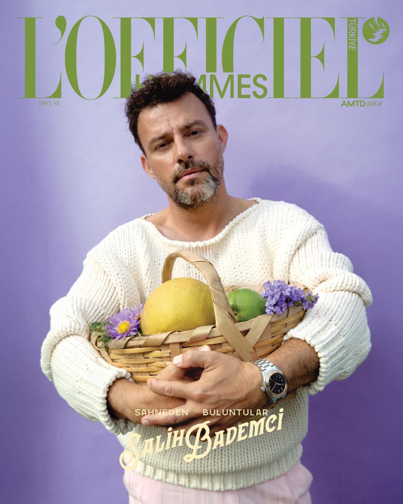 Magazine cover of a man holding a basket with fruit and flowers, wearing a sweater, with the text "L'Officiel Hommes" visible.