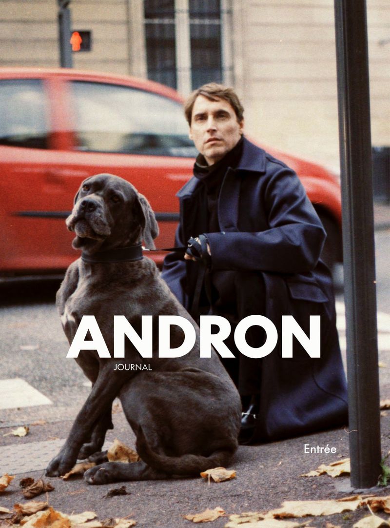 Man and a large dog, possibly a Cane Corso, posing on a city sidewalk near a red car, featured on the cover of a journal.