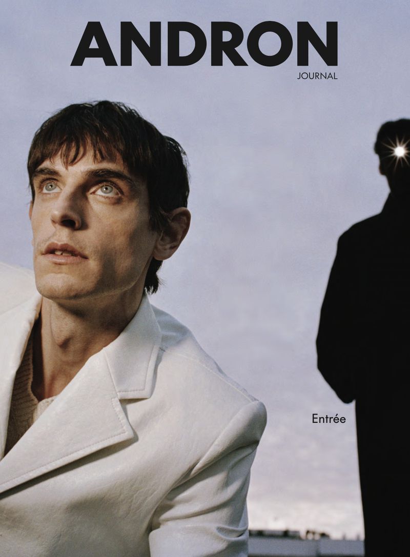 Magazine cover featuring an adult male in a white jacket posing in front of a sky background with a partially silhouetted person.