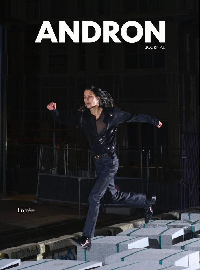 Model in a black shirt and trousers leaping across stacked concrete blocks at night outdoors