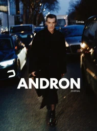 Man wearing a black coat walking on a city street at dusk amidst cars, featured in Andron Journal Spring 2025 Covers.
