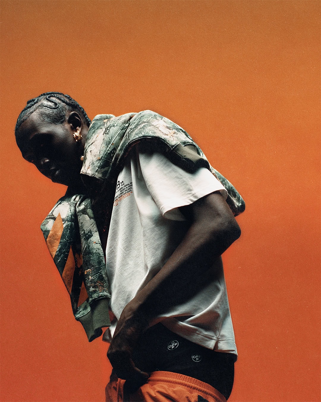 Model wearing a white t-shirt and printed jacket draped over the shoulders against a bold orange backdrop.