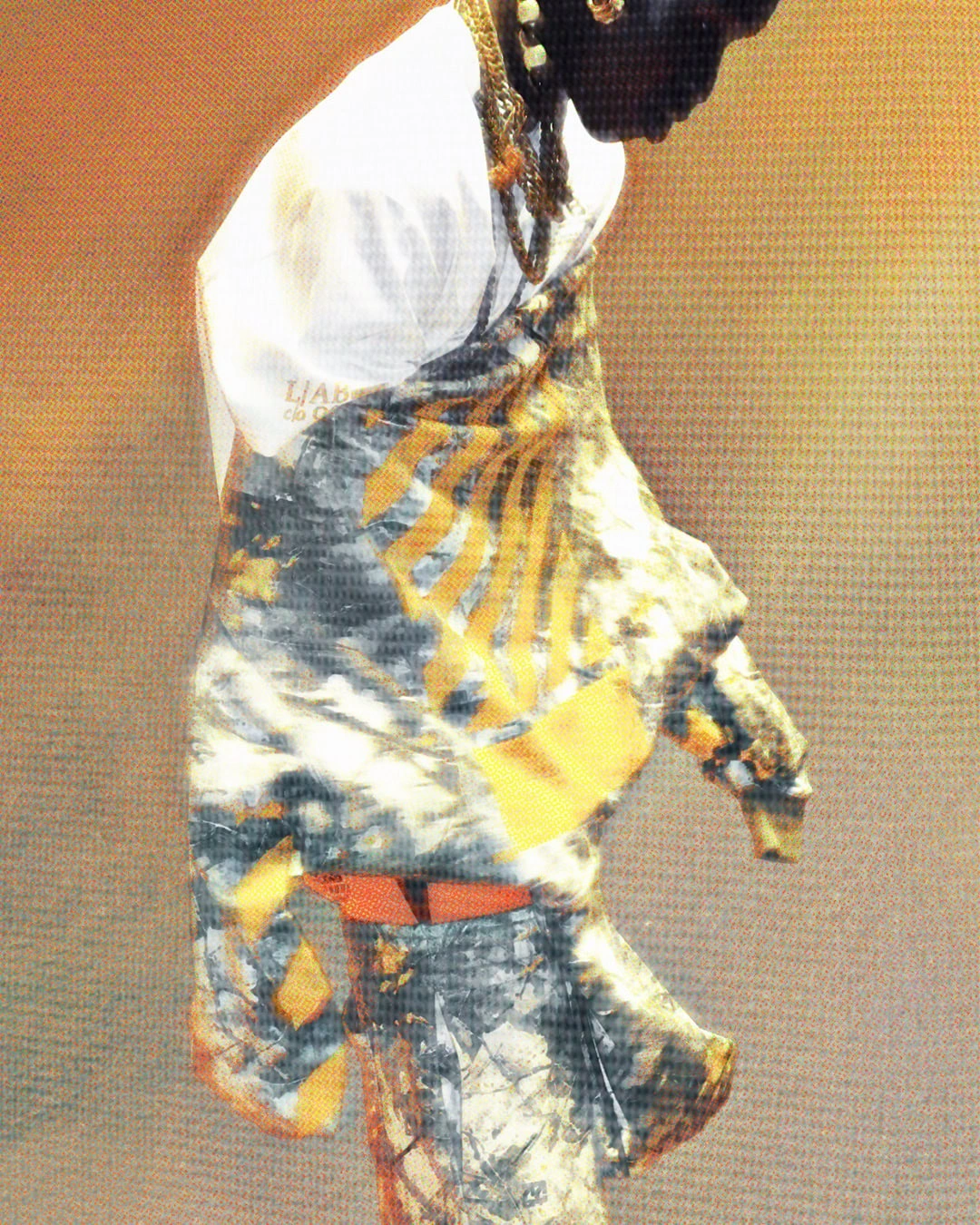 Model wearing a yellow and grey printed graphic wrap over a white shirt and beaded necklace against a warm backdrop.