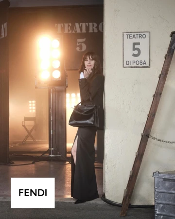 Monica Bellucci in a black slit dress holding a black leather Fendi Peekaboo handbag on a film soundstage set.