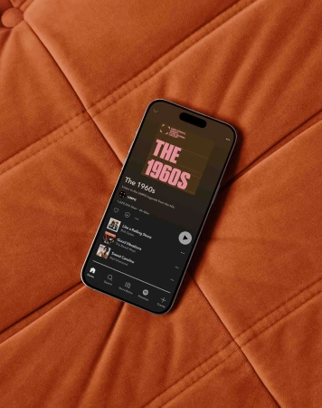 Smartphone displaying a music app interface resting diagonally on an orange tufted quilted surface