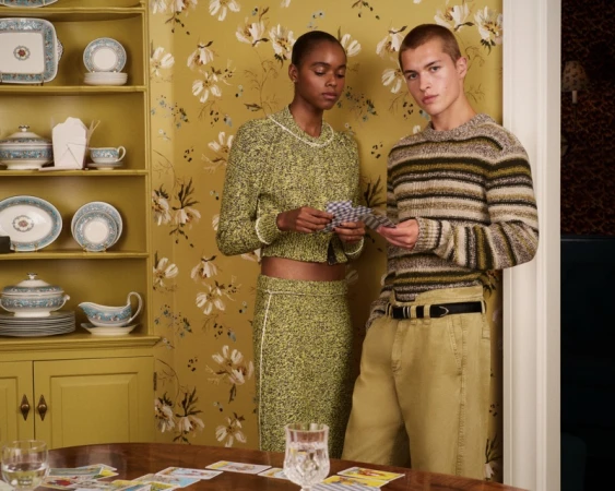 Two models holding playing cards in a yellow floral room for the J.Crew and Eckhaus Latta collaboration campaign.