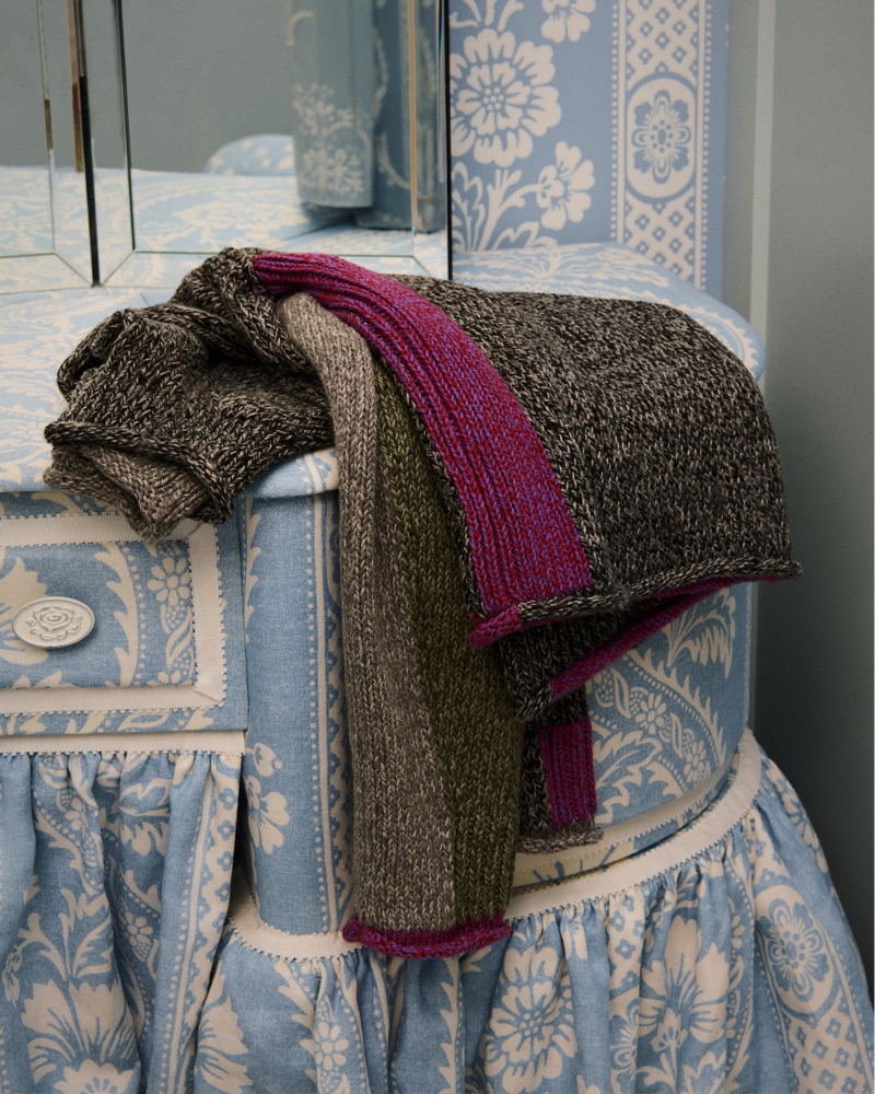 Folded textured knit scarves in grey, green, and magenta resting on blue and white patterned fabric furniture.