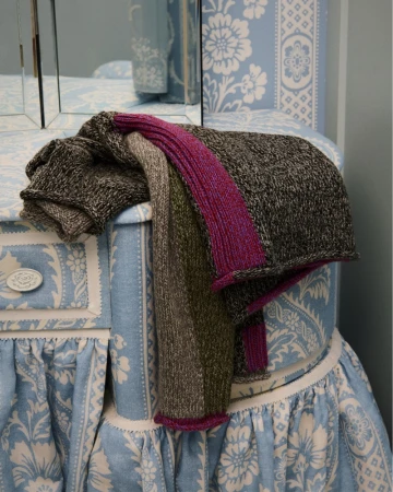 Folded textured knit scarves in grey, green, and magenta resting on blue and white patterned fabric furniture.