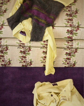 Folded yellow shirt and striped mohair vest resting on a patterned upholstered surface with matching yellow trousers below.